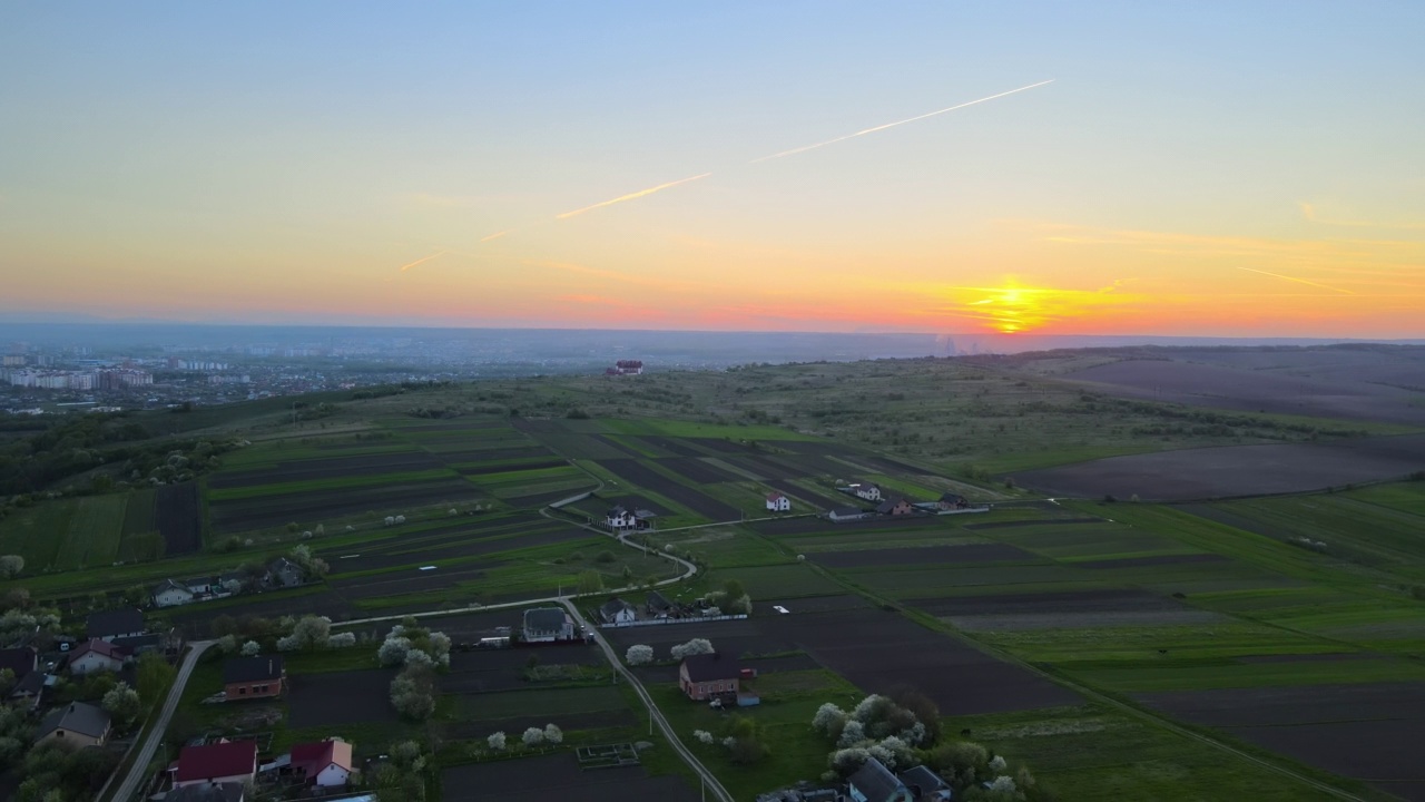 在明亮的夏夜，绿色耕作的农田和远处的村庄房屋的空中景观视图视频素材