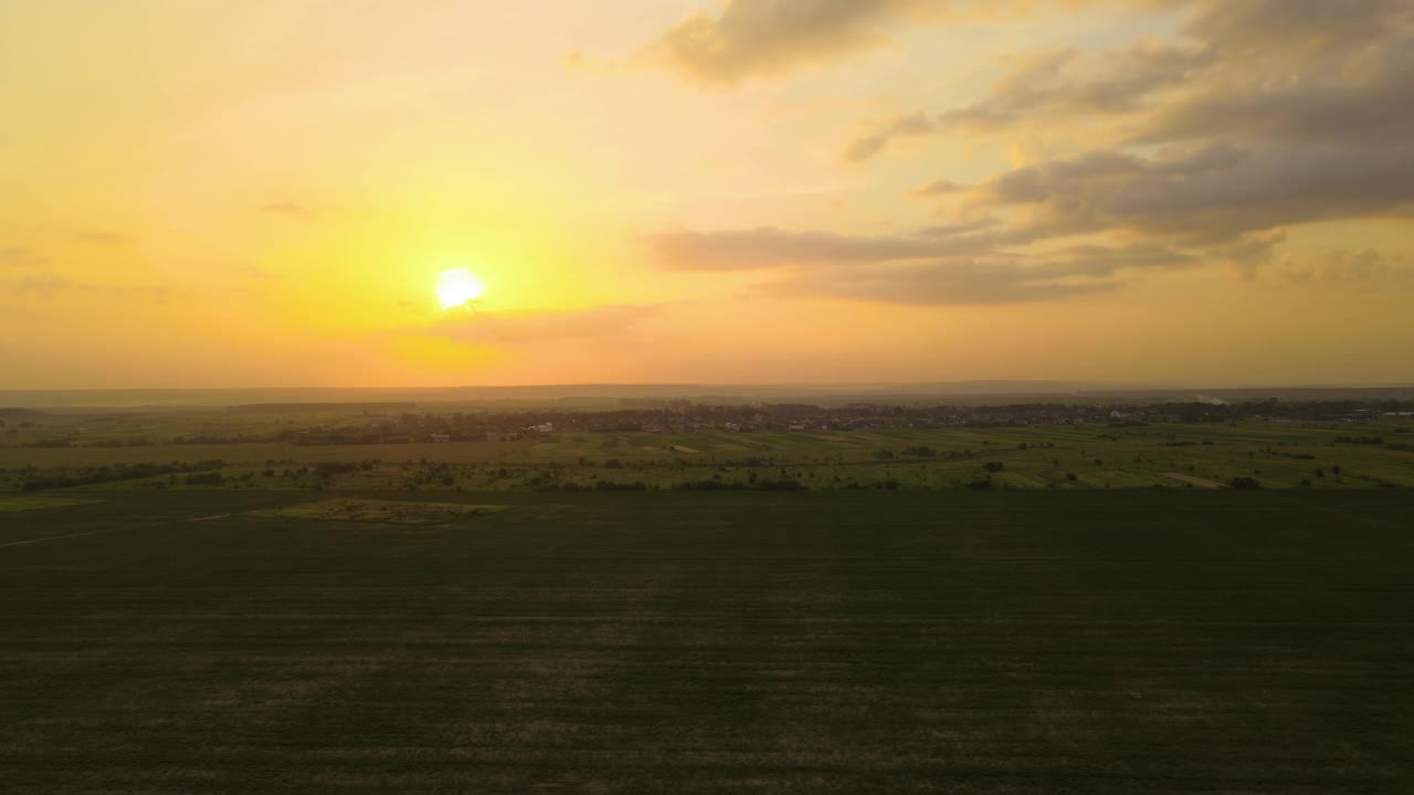 在明亮的夏夜，绿色耕作的农田和远处的村庄房屋的空中景观视图视频素材