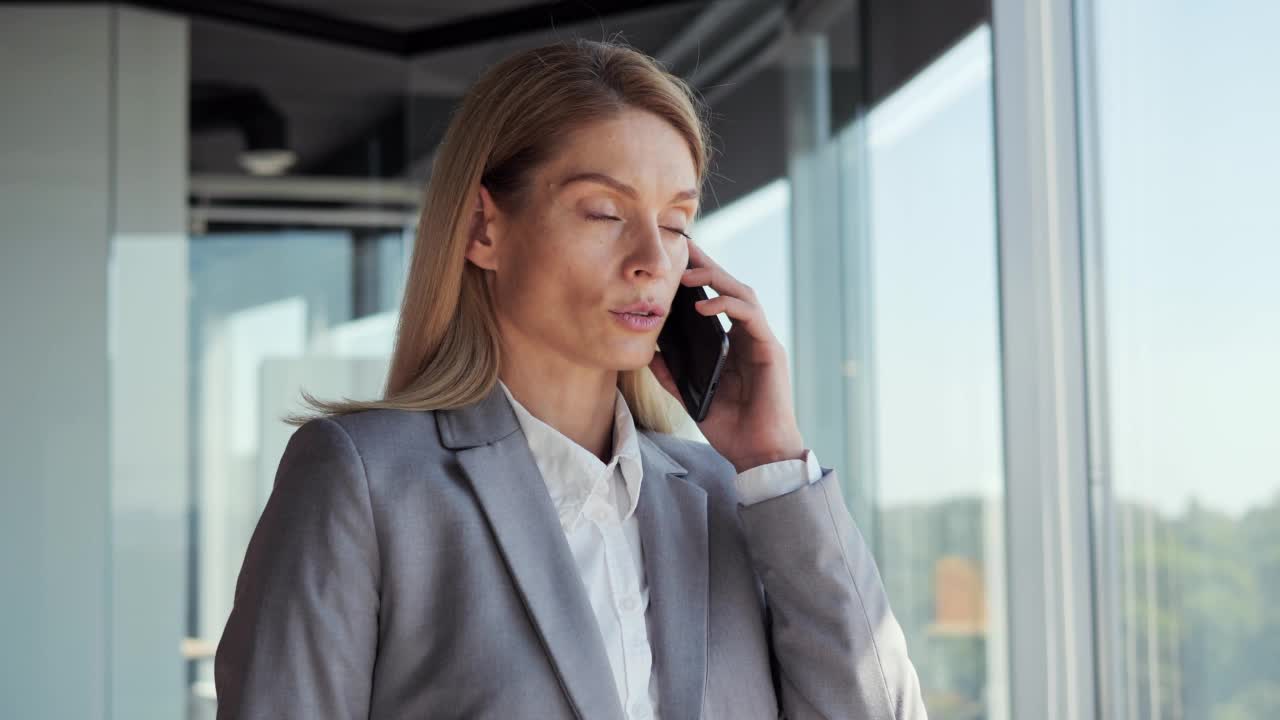 专注的女商人在办公室讲手机。严肃的经理肖像在室内用智能手机交谈。商界女性CEO会解决这些问题。成功的公司女性领导者。视频素材