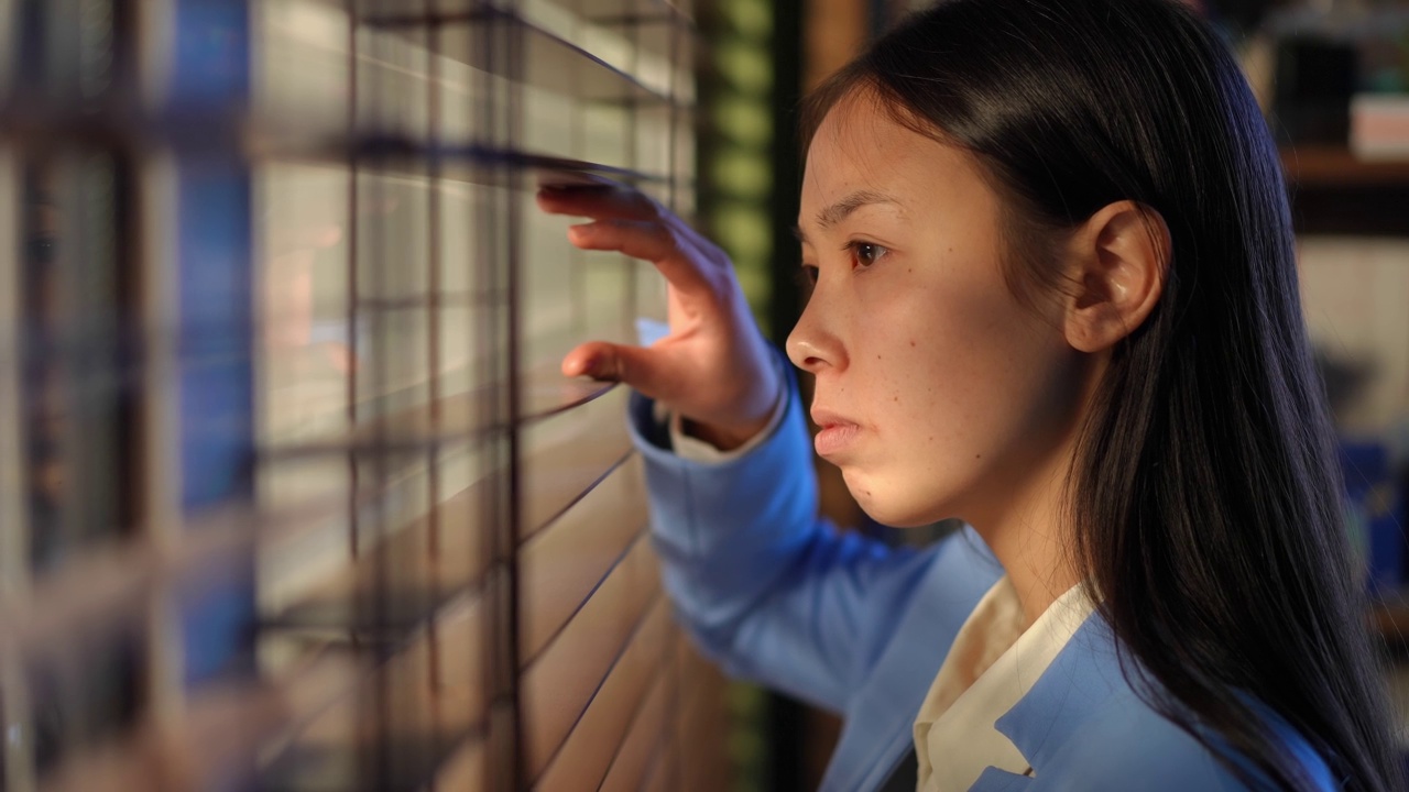 侧视图亚洲年轻女子触摸眼罩看窗外在办公室和离开。苗条迷人的女经理穿着优雅的西装在早上开始一天的工作。视频素材