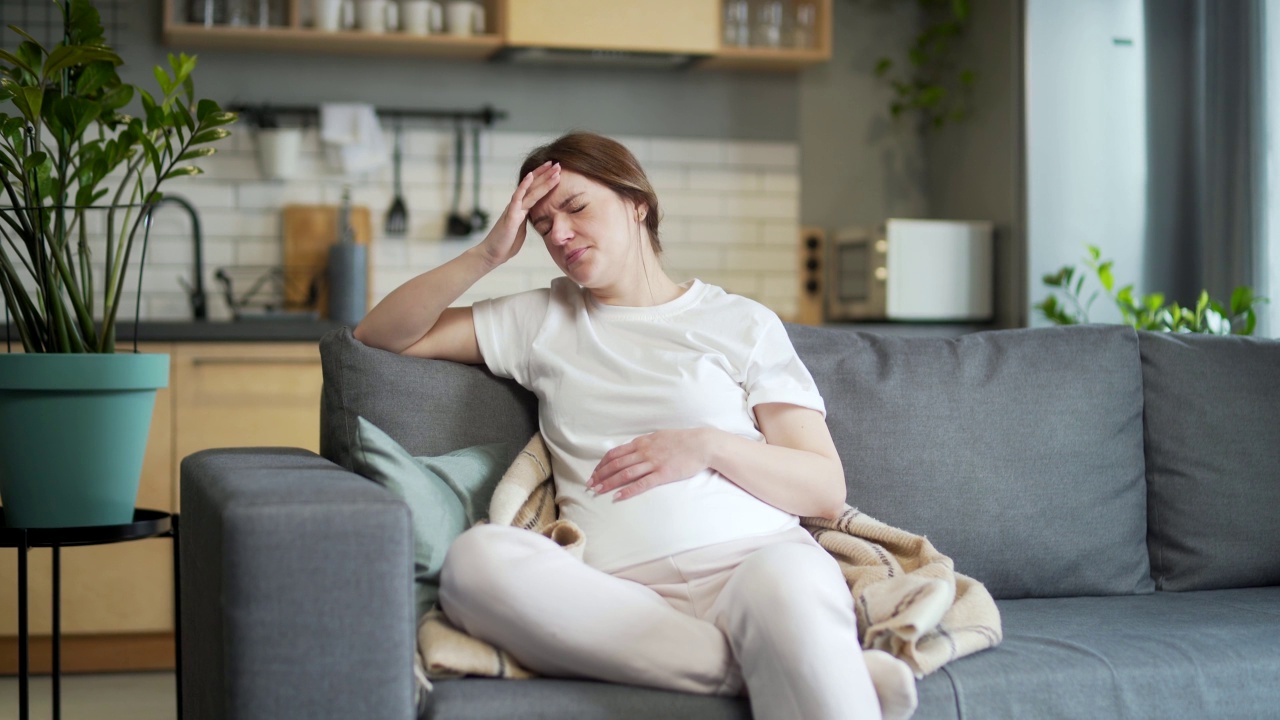 孕妇，身体不适。早上生病回家头痛，怀孕时抑郁坐在客厅沙发上。室内。女性的担忧、焦虑视频素材