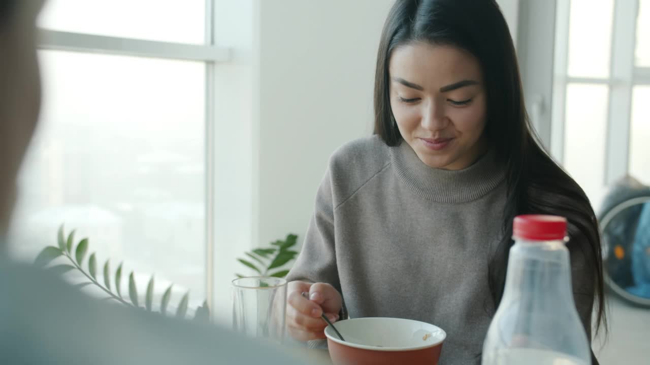 快乐的亚洲女人早餐吃麦片，在家里的厨房微笑着和丈夫说话视频素材