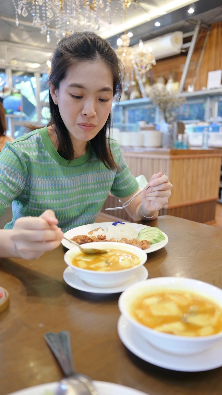 亚洲女性在餐厅吃泰国菜橙咖喱炒猪肉和jusmine饭视频素材