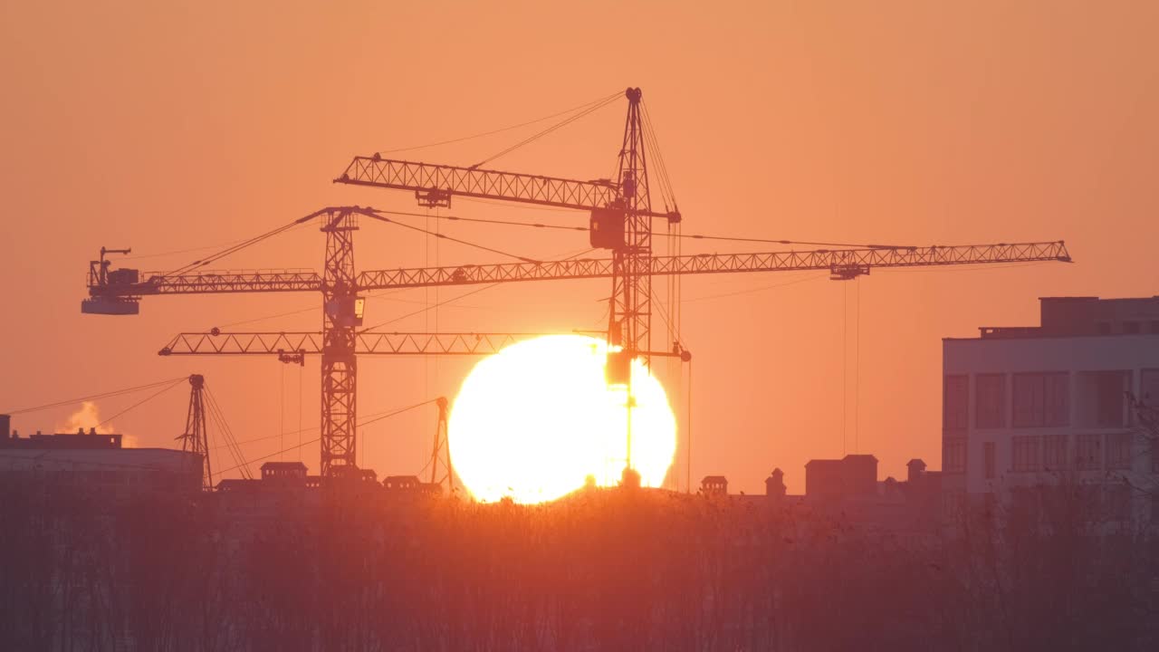 夕阳西下，高层住宅楼施工现场塔吊的黑色剪影。房地产开发视频素材