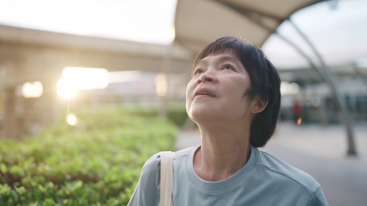 一名亚洲女子站在户外呼吸新鲜空气时摘下防护口罩。视频素材