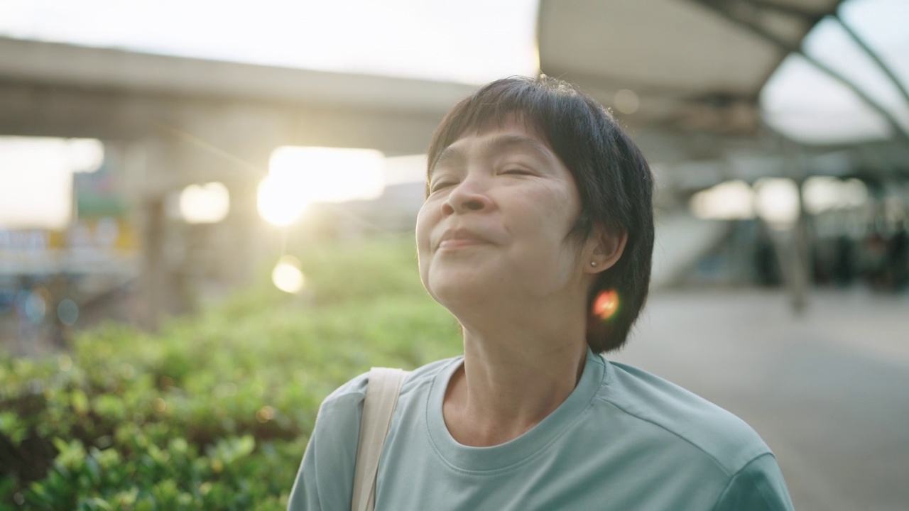 一名亚洲女子站在户外呼吸新鲜空气时摘下防护口罩。视频素材