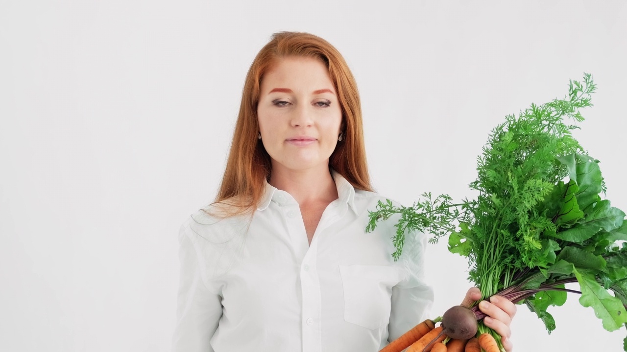 年轻的红发女人与蔬菜在白色的背景。素食的女人视频素材