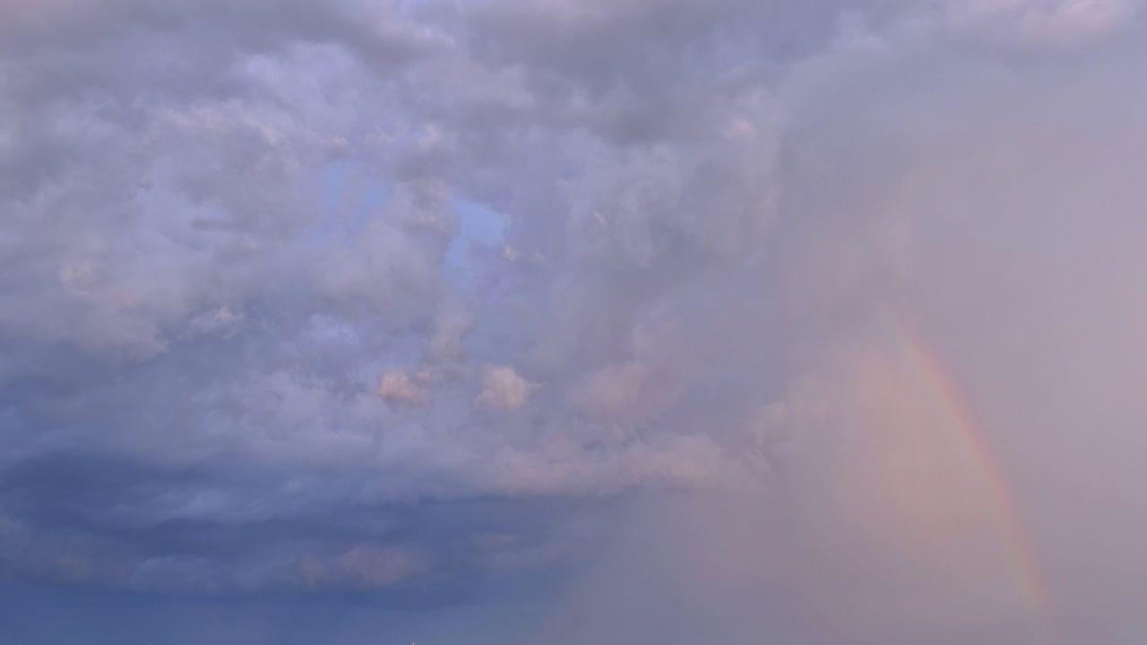 在一场强烈的雷雨中，天空中点缀着一道明亮的彩虹，与周围的风景形成鲜明的对比视频素材