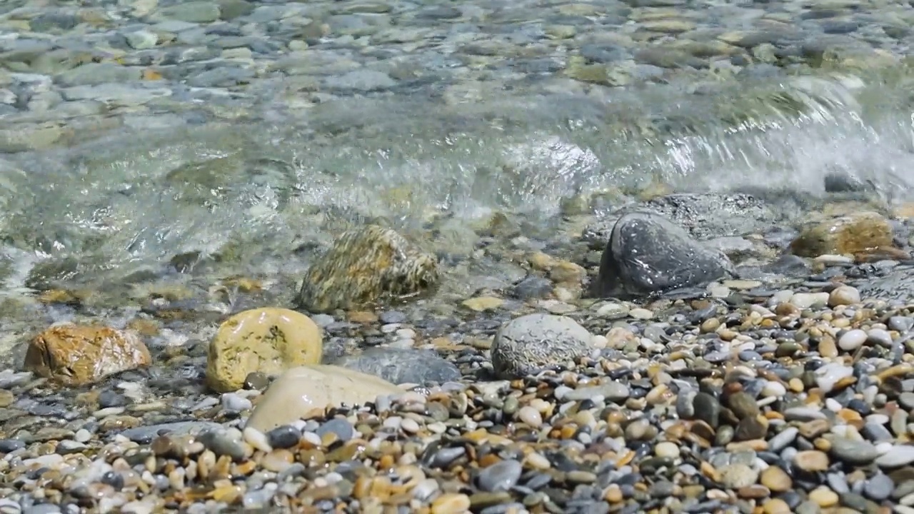 卵石滩上的海浪。清澈的水波流过卵石滩岸边视频素材