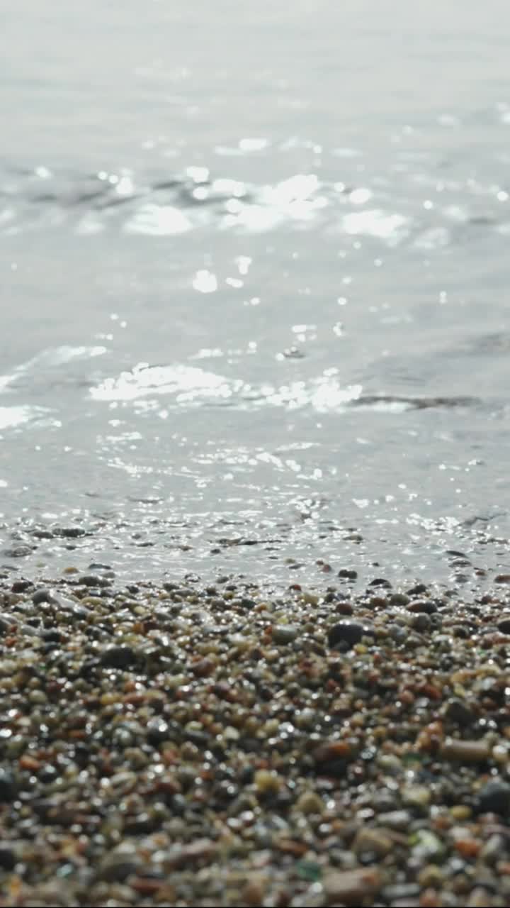 圆石滩，透明的波浪，阳光照射在水面上。靠近多石的海岸。海浪带平静大海的自然背景。移到右边视频素材