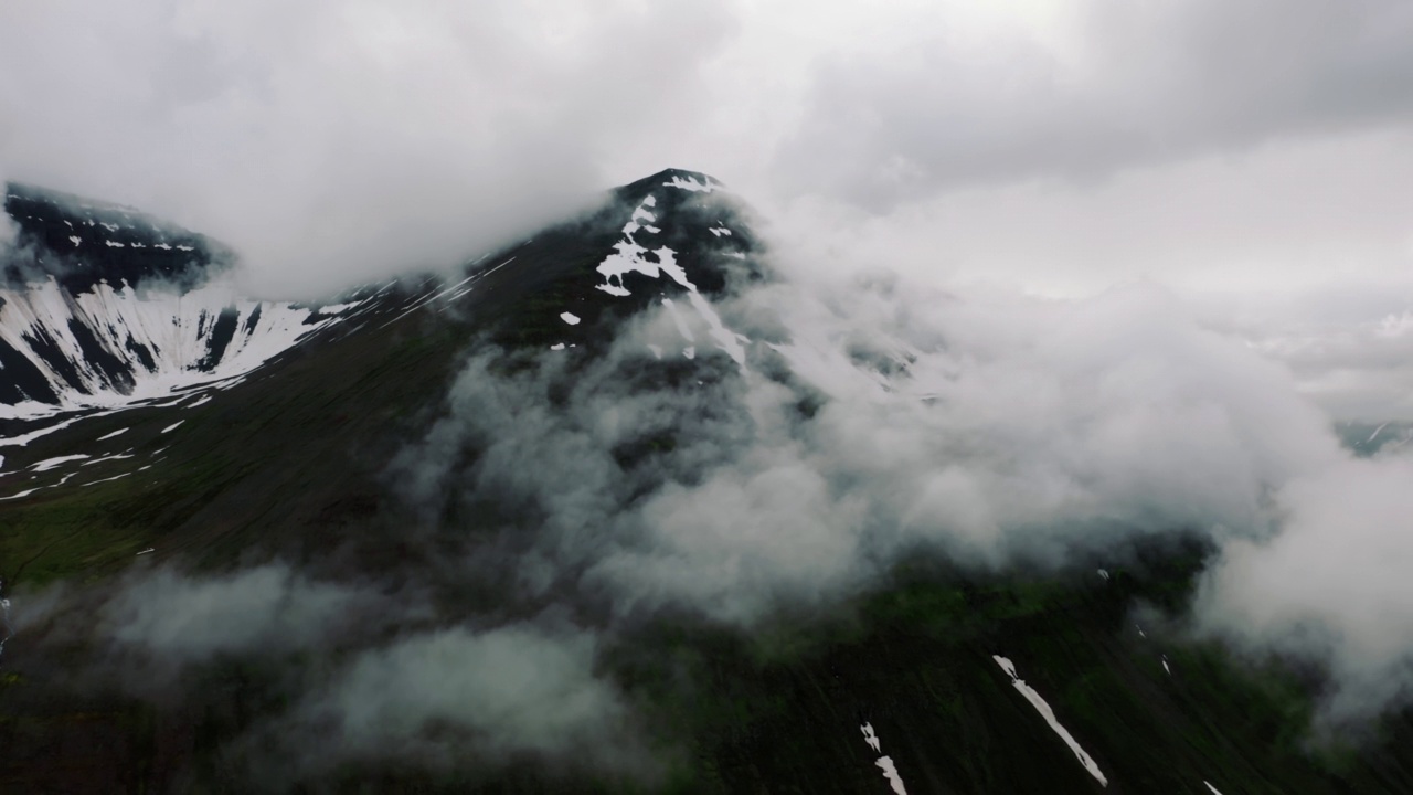 鸟瞰北欧景观，飞越美丽的雪山覆盖着连绵的雨云，冰岛美丽的形成。无人机拍摄的惊人的北部悬崖视频素材