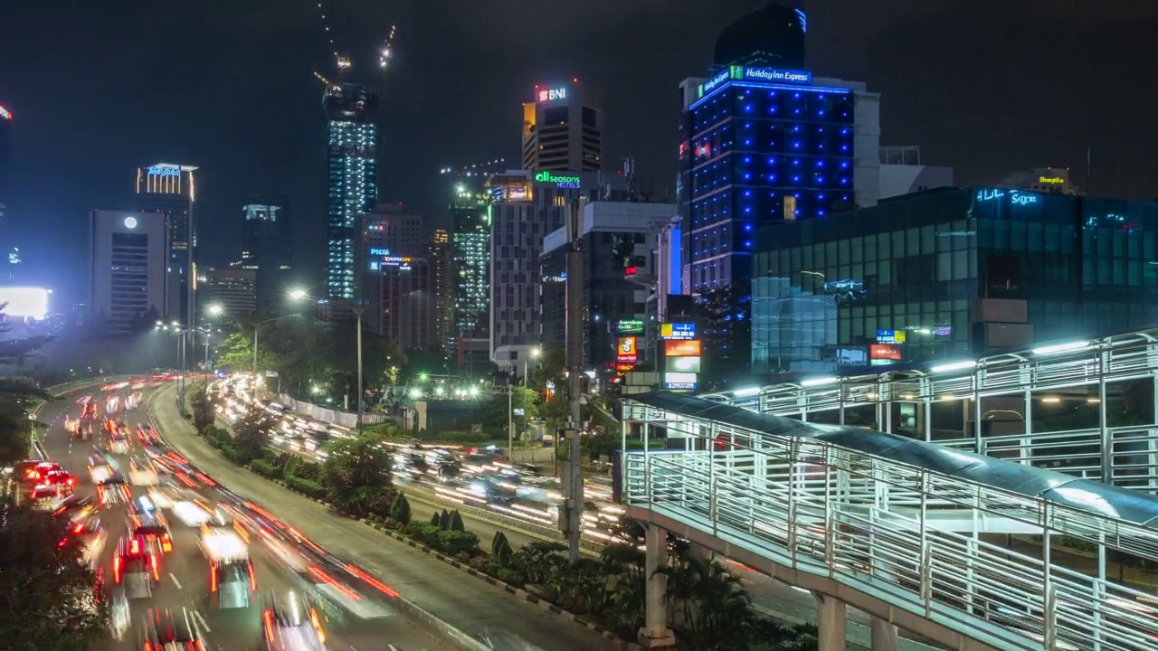 印尼首都和最大城市雅加达的现代天际线前的夜间交通延时视图，放大视频素材