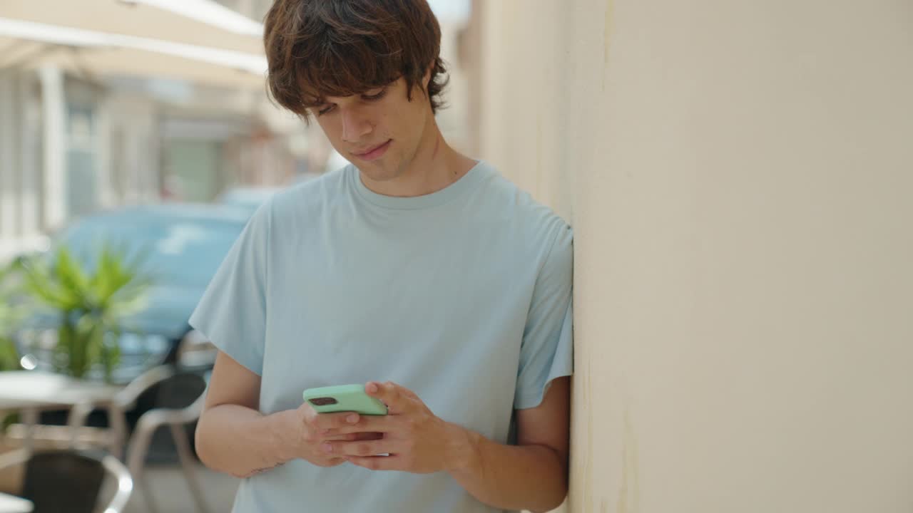 年轻的金发男子微笑着自信地在街上用智能手机自拍视频素材