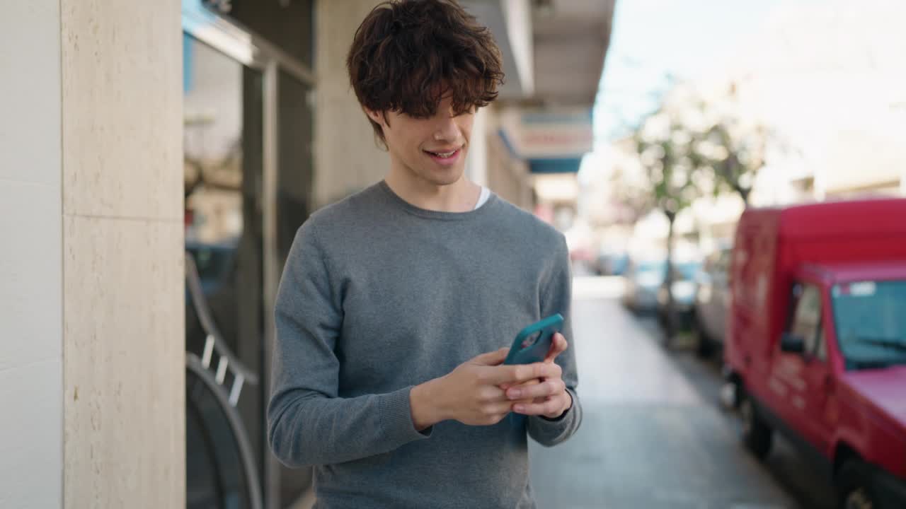 年轻的西班牙裔男子自信地微笑着在街上使用智能手机视频素材