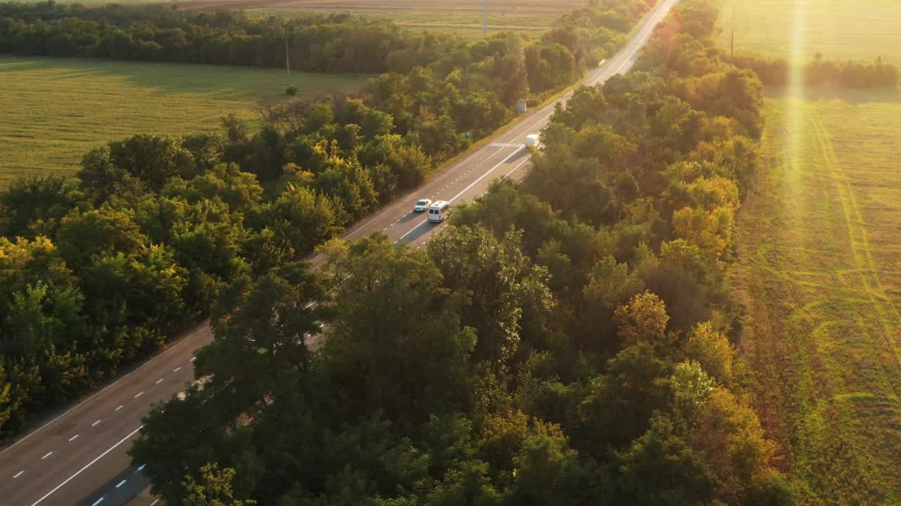 航拍的一辆谷物卡车在夏日夕阳下行驶在美丽的乡村道路上。无人机拍摄的卡车行驶在乡间的高速公路上，沿途有农田和树木。视频素材