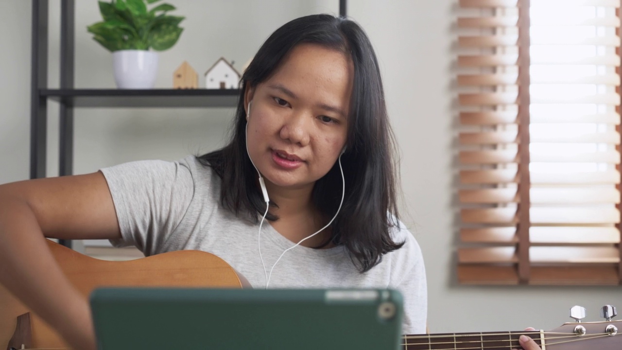 亚洲妇女练习打原声吉他学习在线教程在家里。具有技能提升理念的周末活动视频素材