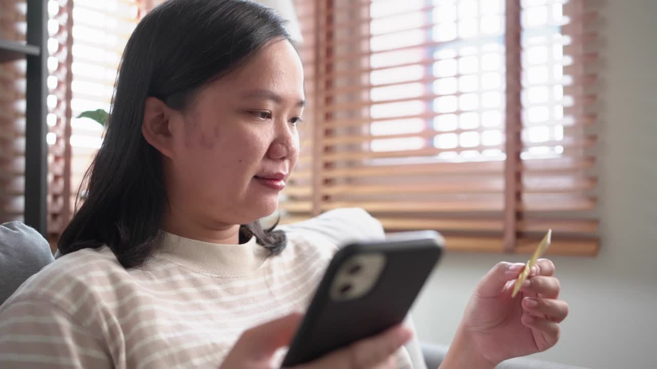 坐在客厅沙发上的女人用智能手机刷卡购物的特写视频素材