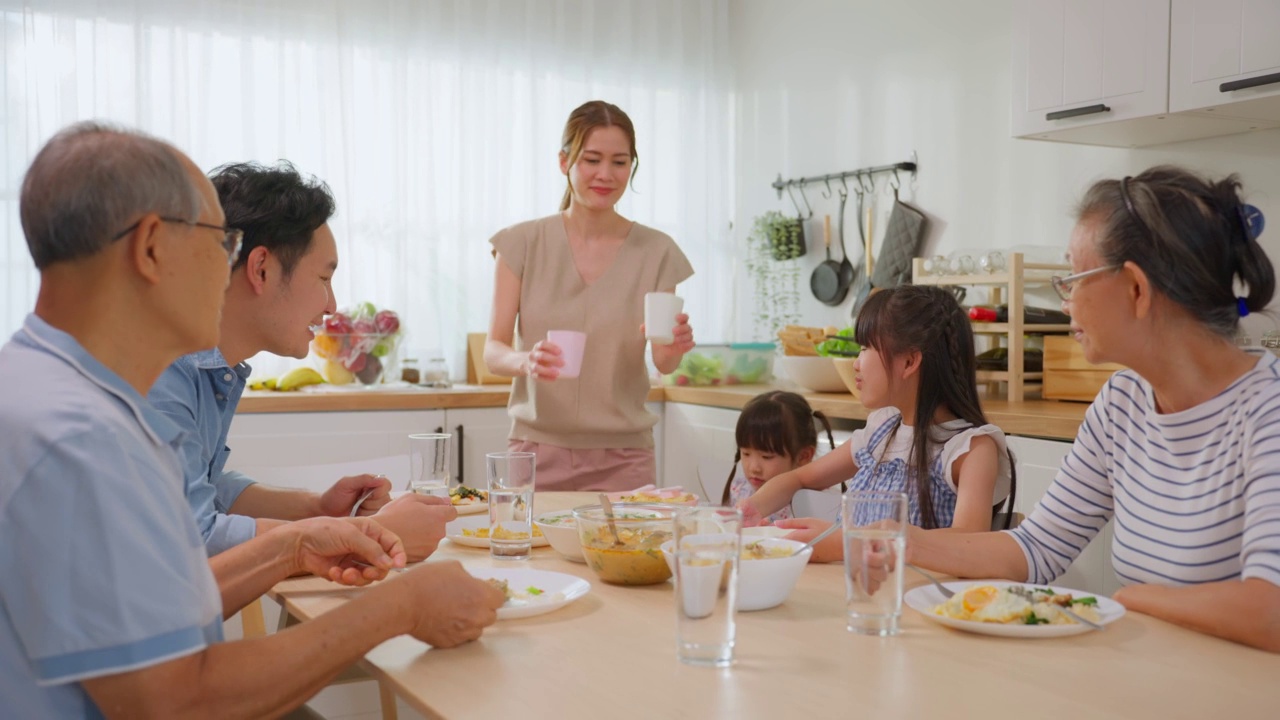 亚洲大家庭在家里的餐桌上共进午餐。年长的祖父母，年轻的夫妇和年幼的孩子女儿感到幸福，享受在家里吃的食物。活动关系的概念视频素材