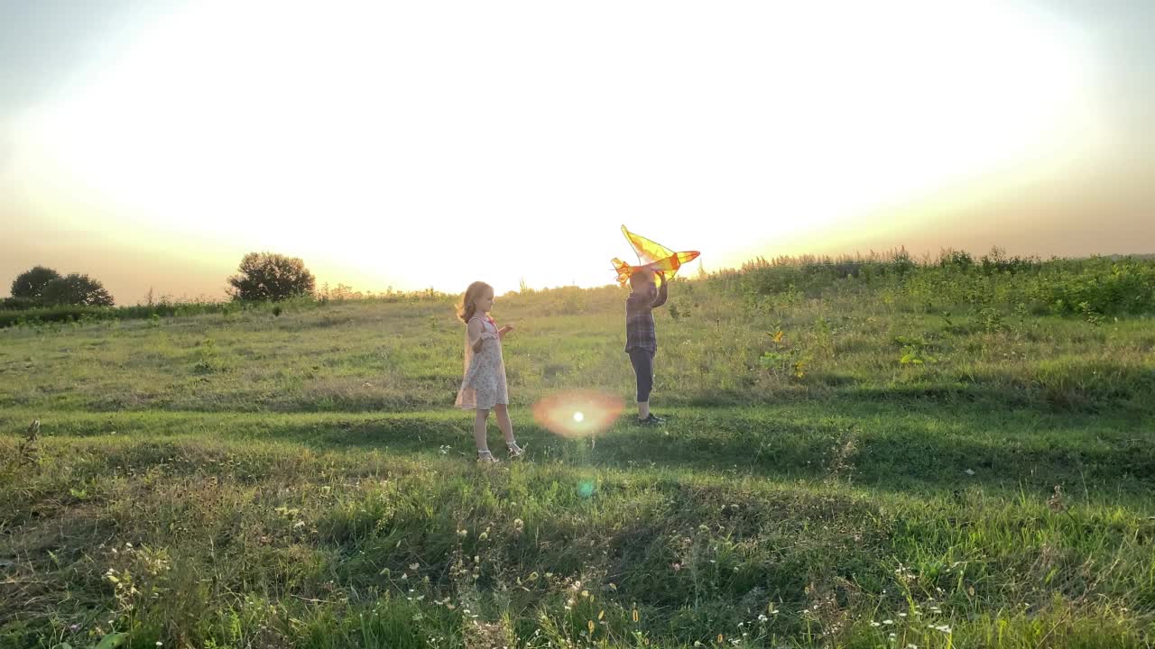 两个孩子准备在夕阳下的草地上放风筝。视频素材