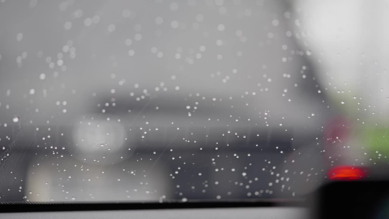 特写汽车风挡玻璃与雨滴和雨刷擦拭在城市交通堵塞视频素材