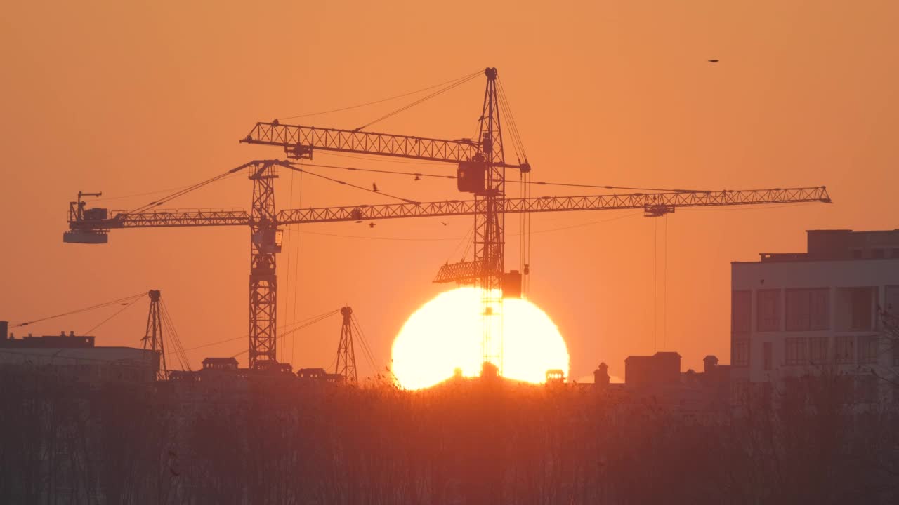 夕阳西下，高层住宅楼施工现场塔吊的黑色剪影。房地产开发视频素材