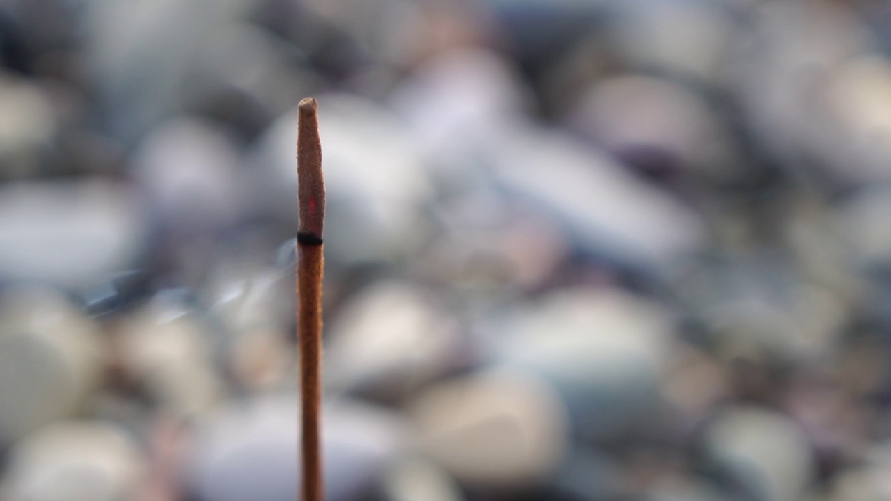 近景香香扑鼻的香棒燃烧在卵石滩岸边。小波浪在水面上运动模糊与散景灯从日出。冥想的概念。慢动作视频素材