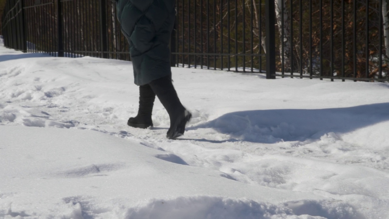 穿着冬季鞋的女人的腿沿着城市公园的雪道行走。冬日公园里，穿着暖和靴子的女人在雪地里行走视频素材