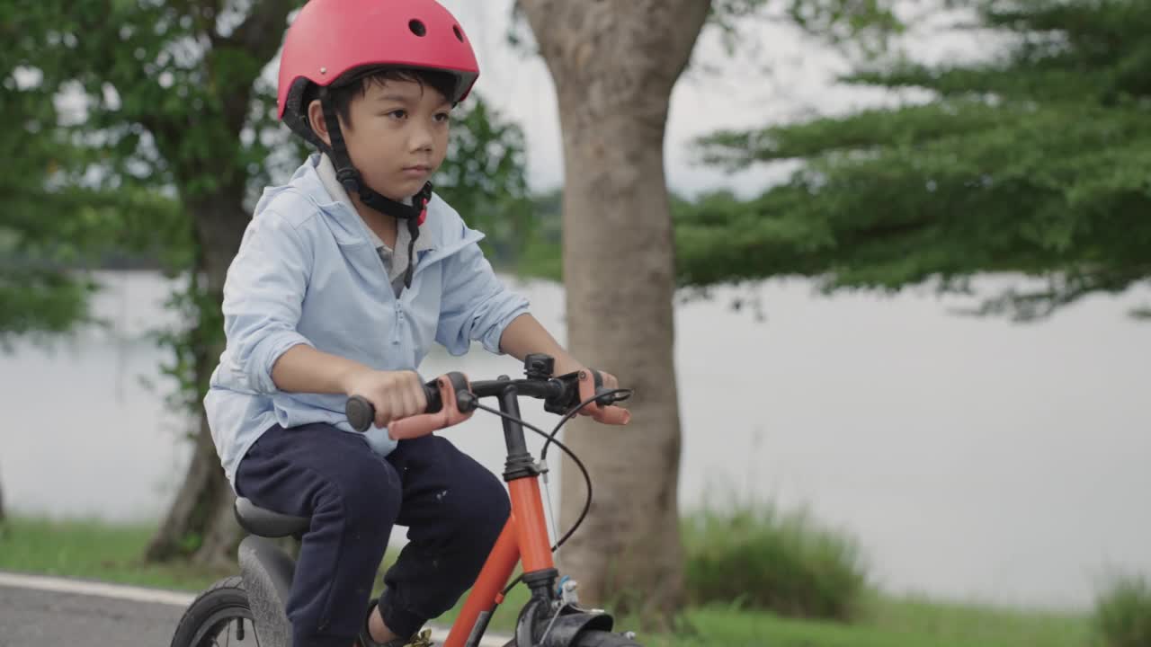 男孩，孩子，戴着安全帽在城市公园里快乐地学习骑自行车视频素材