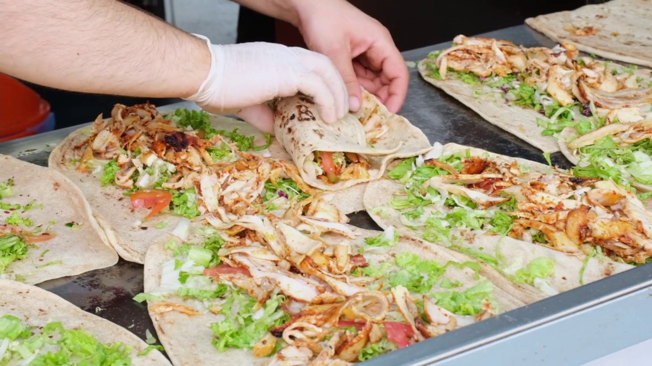 垃圾食品和户外饮食的概念。一名男子在白天的露天街市上做传统的卷饼，售卖当地美食和小吃。视频素材