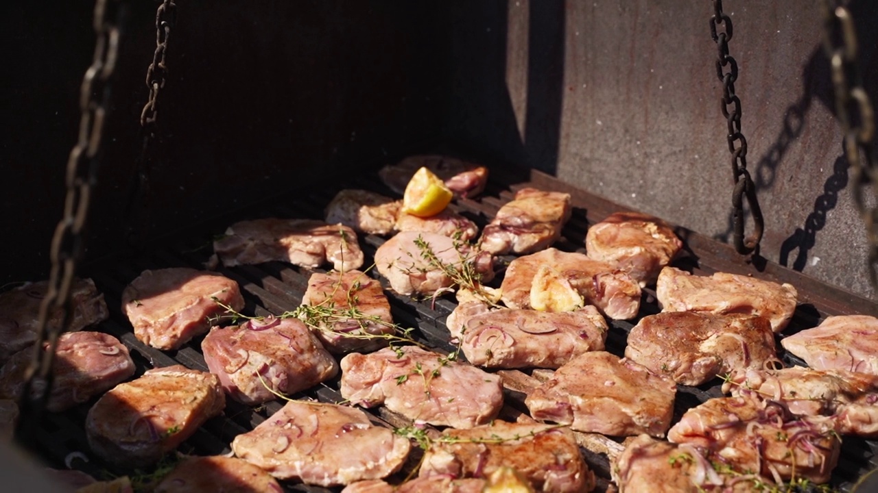 特写厨师煎肉在一个大型工业炉烧烤户外餐饮服务。厨师把调味料和香草倒在炸猪肉上。视频素材