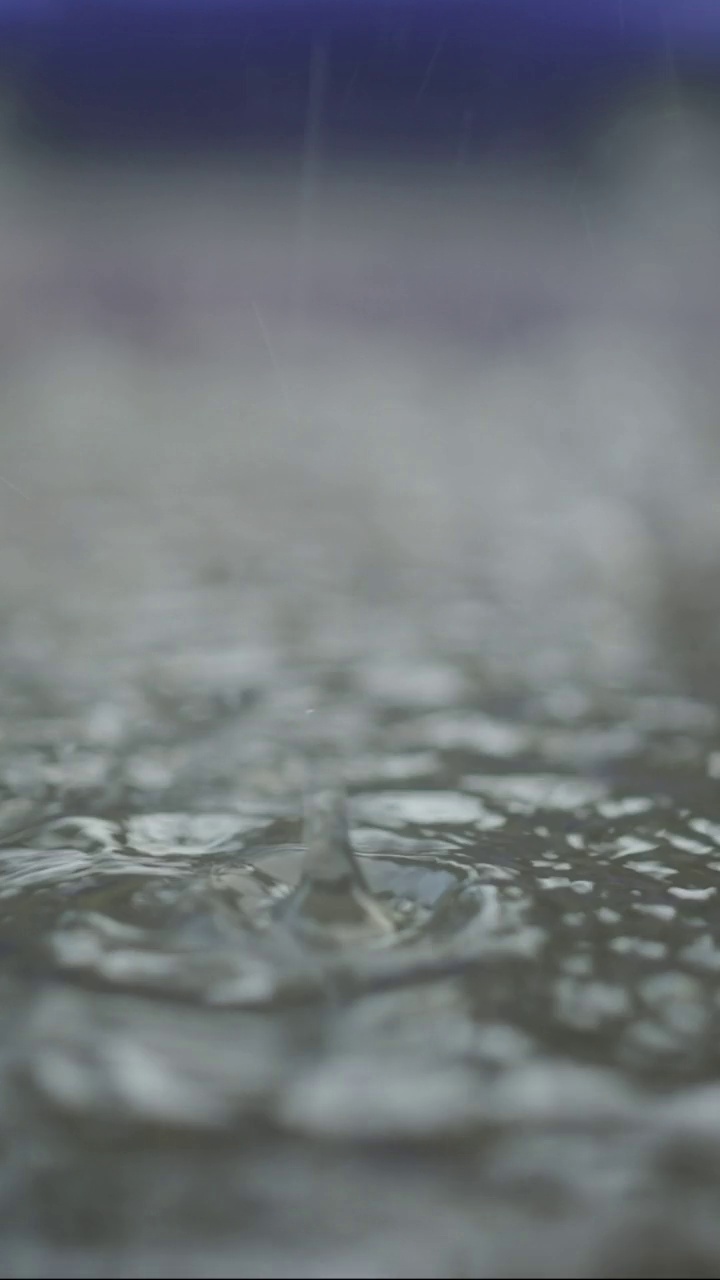 垂直视频:雨滴落入人行道上的水坑的极端特写，汽车在背景中行驶。城里下起了倾盆大雨。视频素材