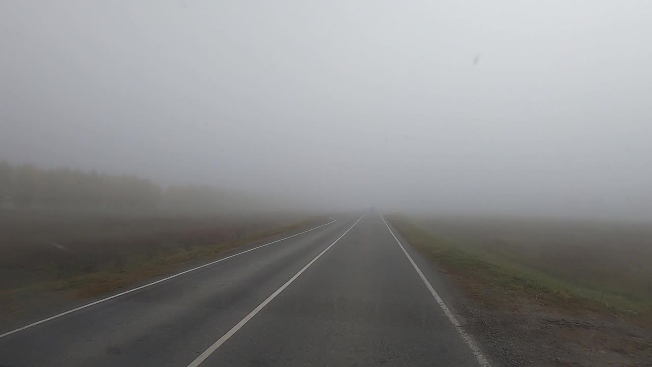 汽车在空旷、雾蒙蒙、能见度低的郊区高速公路上行驶。透过挡风玻璃射击视频素材