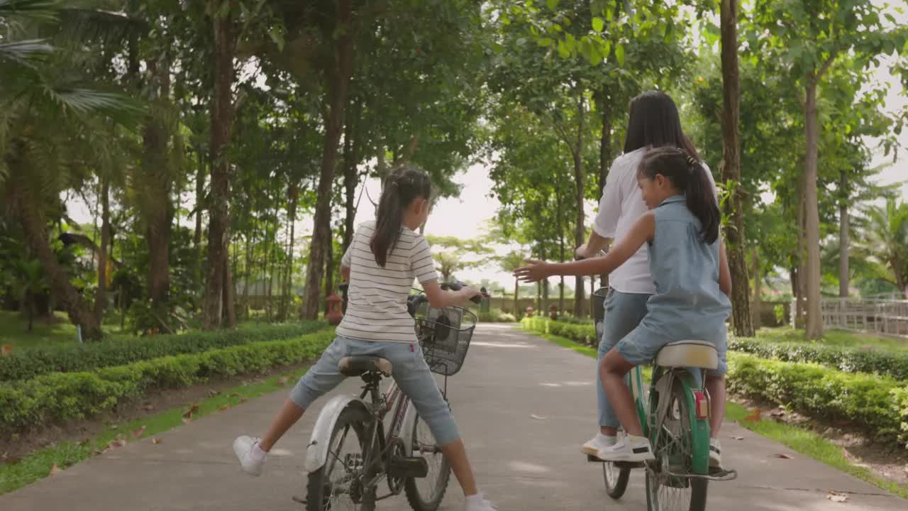 亚洲母亲和两个孩子骑着自行车，快乐地在花园里户外骑行。一家人一起度假，享受大自然的生活方式。视频素材