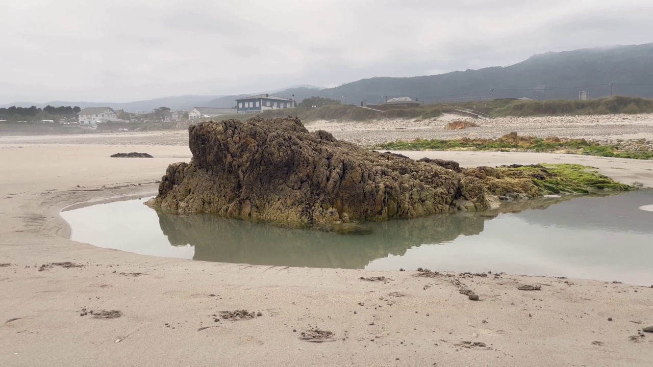 海滩上的场景，岩石被水包围。背景中的房屋和道路。视频素材