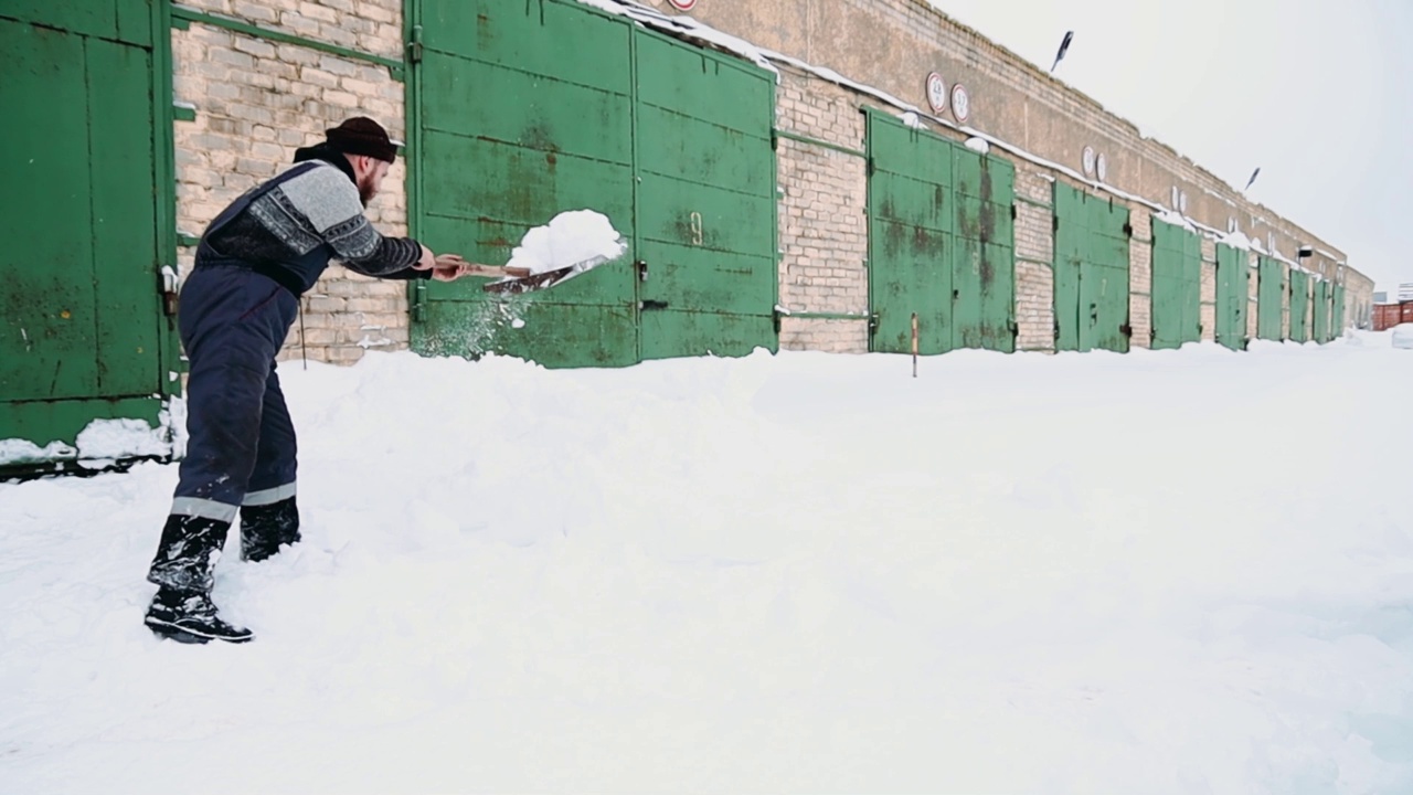 一名男工人在工厂车库门口清理积雪。用铲子进行体力劳动的概念。视频素材