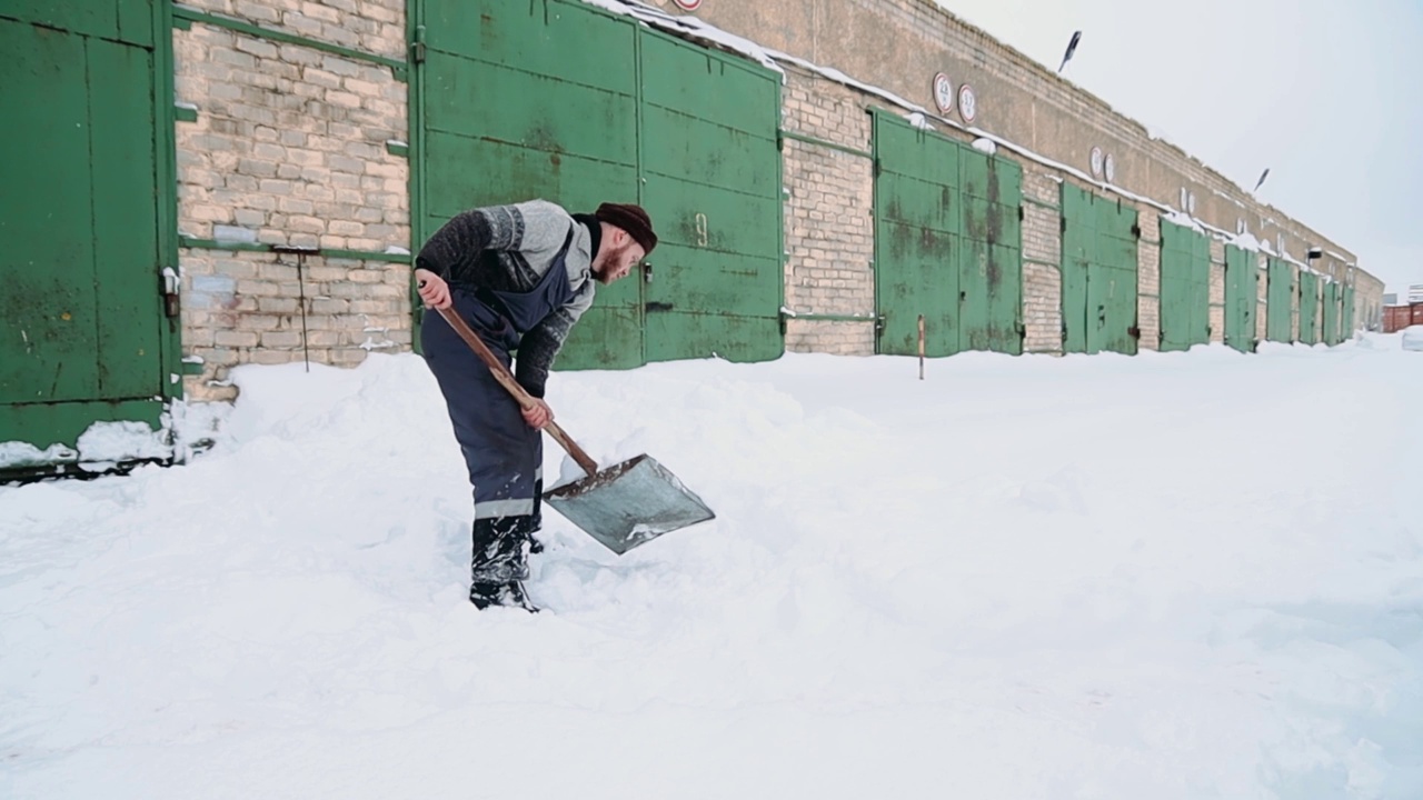 一名男工人在工厂车库门口清理积雪。用铲子进行体力劳动的概念。视频素材