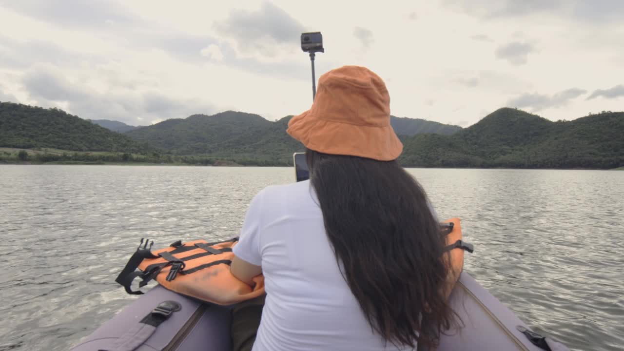 后视图快乐的年轻女子在皮划艇上拍照或自拍在水的大山湖。夏季旅游，探险，度假的概念。视频素材