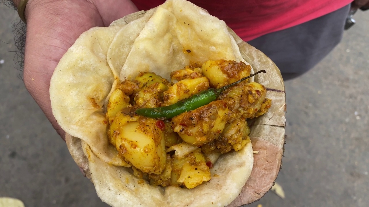 一名男子端着一盘几个pooris，每一盘都配有油炸绿辣椒和麻辣的masala Aloo Dum。视频素材