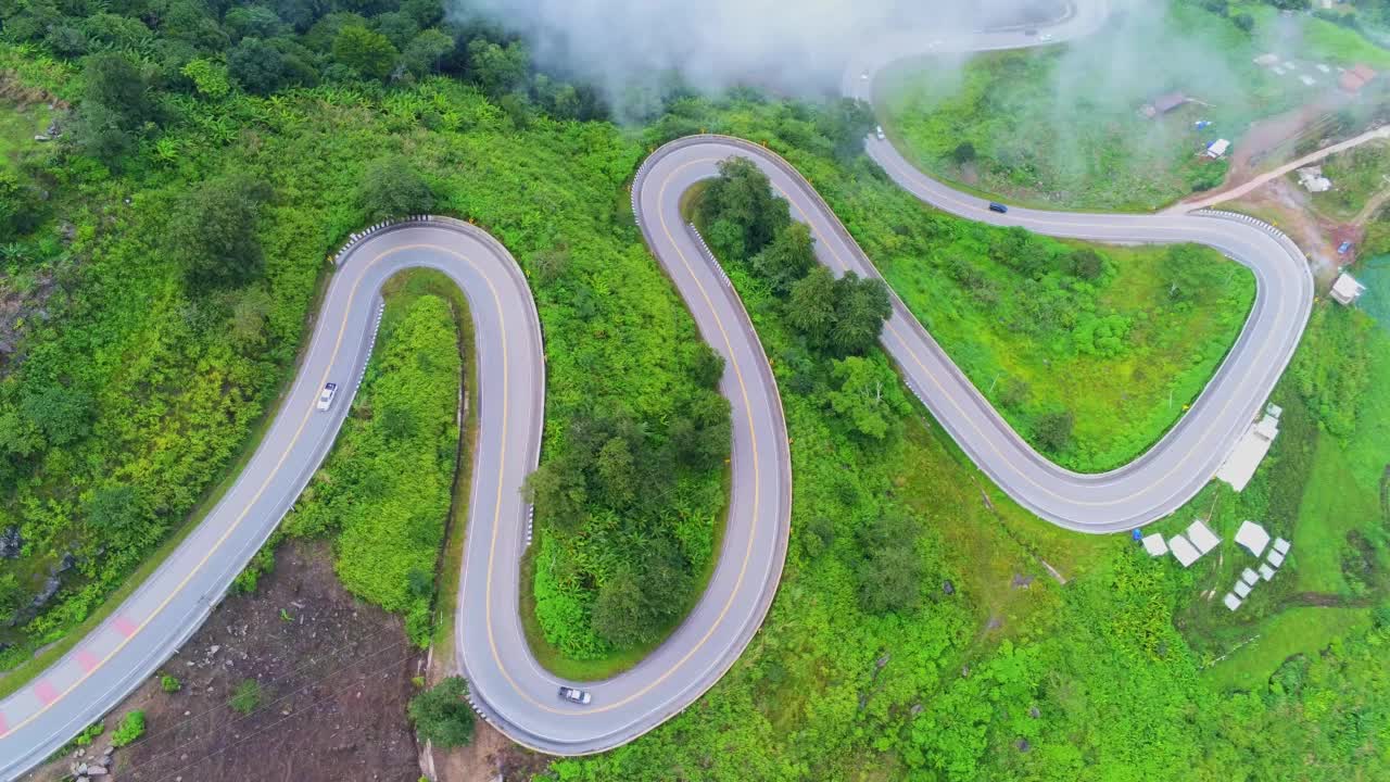 空中视频俯视图无人机道路照片在绿色山脉与白色雾漂浮和路径令人兴奋的陡峭道路的旅行方式。视频素材