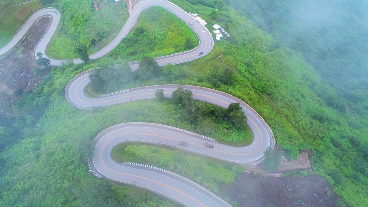 空中视频俯视图无人机道路照片在绿色山脉与白色雾漂浮和路径令人兴奋的陡峭道路的旅行方式。视频素材