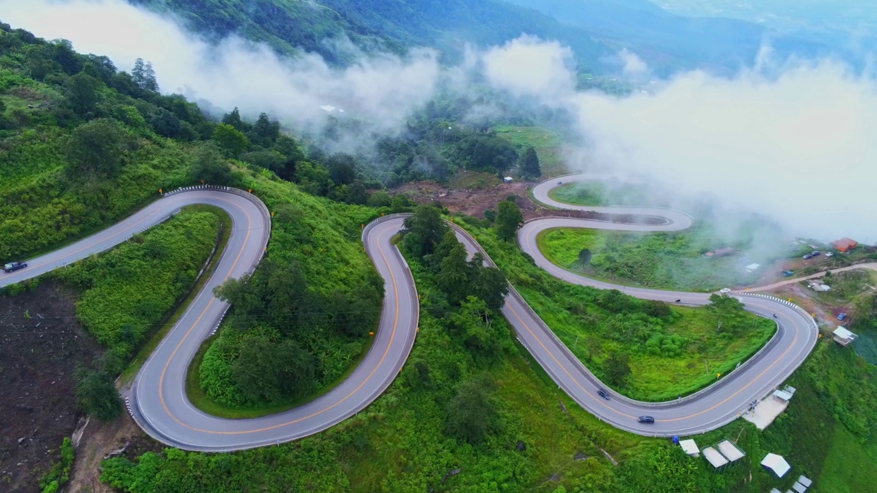 空中视频俯视图无人机道路照片在绿色山脉与白色雾漂浮和路径令人兴奋的陡峭道路的旅行方式。视频素材