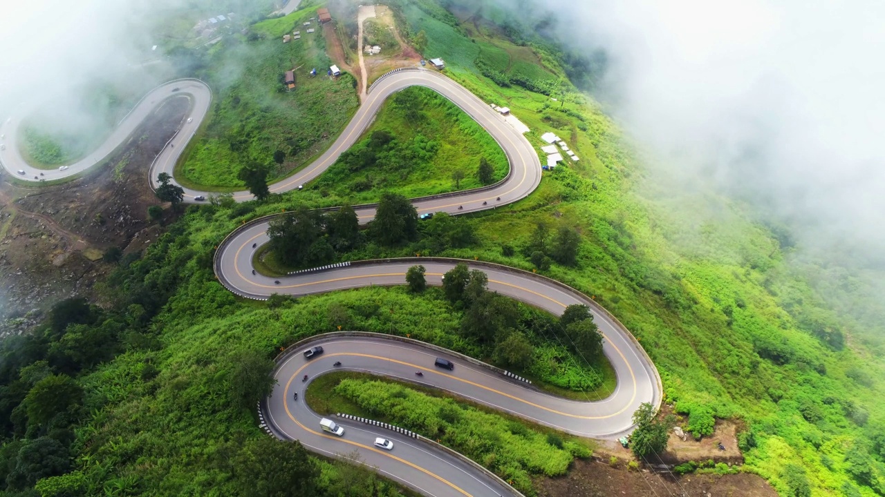 空中视频俯视图无人机道路照片在绿色山脉与白色雾漂浮和路径令人兴奋的陡峭道路的旅行方式。视频素材