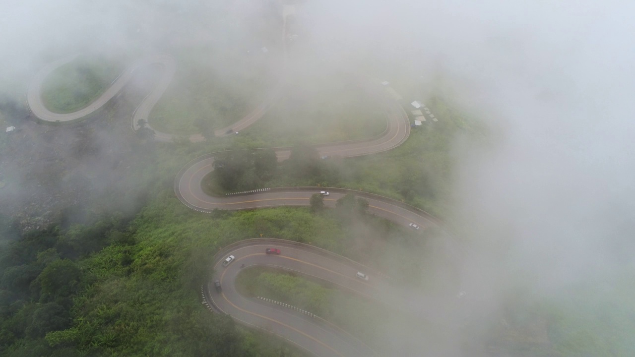 空中视频俯视图无人机道路照片在绿色山脉与白色雾漂浮和路径令人兴奋的陡峭道路的旅行方式。视频素材