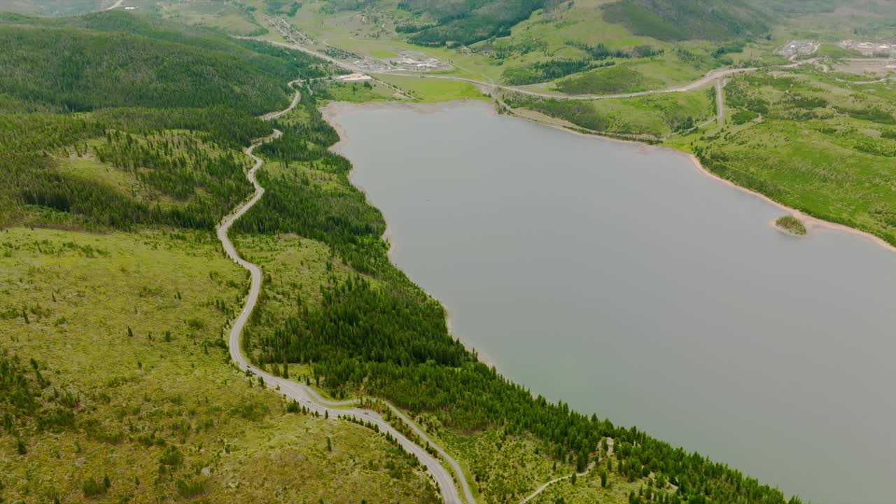 美丽的湖泊位于山区，四周绿意盎然。沿河而行的波浪形交通道路。鸟瞰图。视频素材