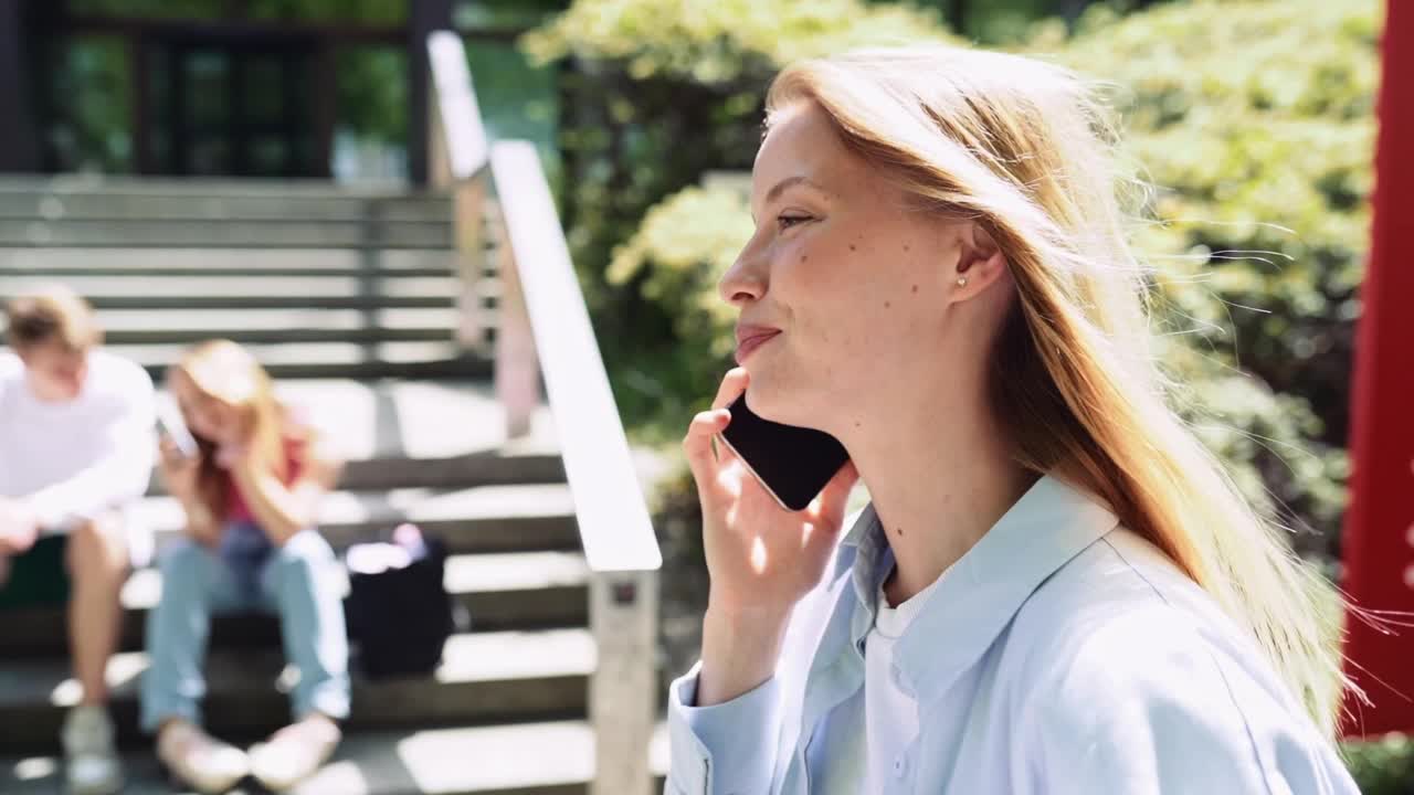 年轻的女学生微笑着打电话走在城市公园外面。视频素材