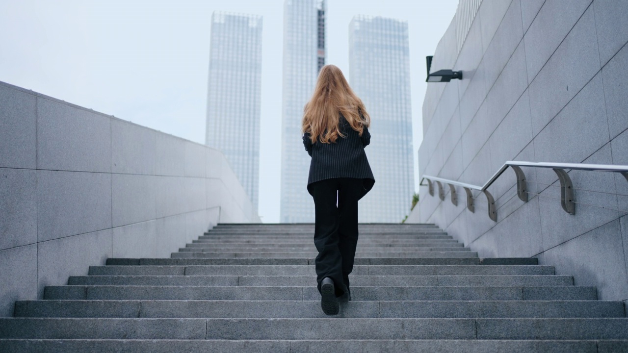 在现代城市建筑的背景下，一位女商人正在爬楼梯。镜头跟随这位攀登职业阶梯的女性视频素材