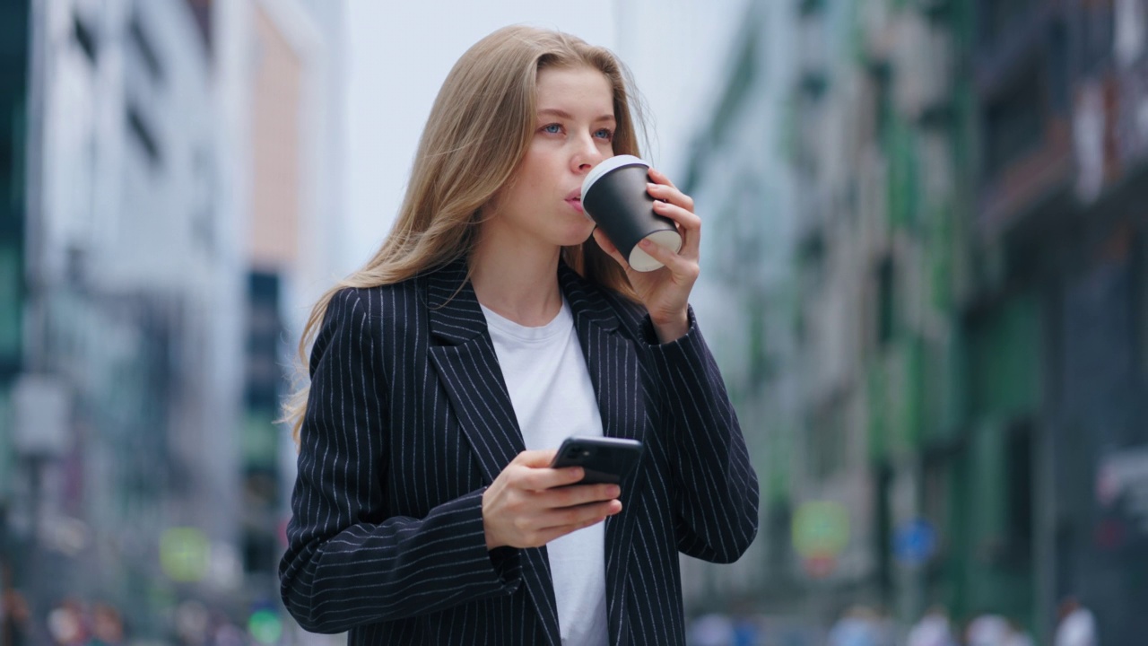 自信和雄心勃勃的女人穿着西装走在市中心，看着智能手机屏幕视频素材