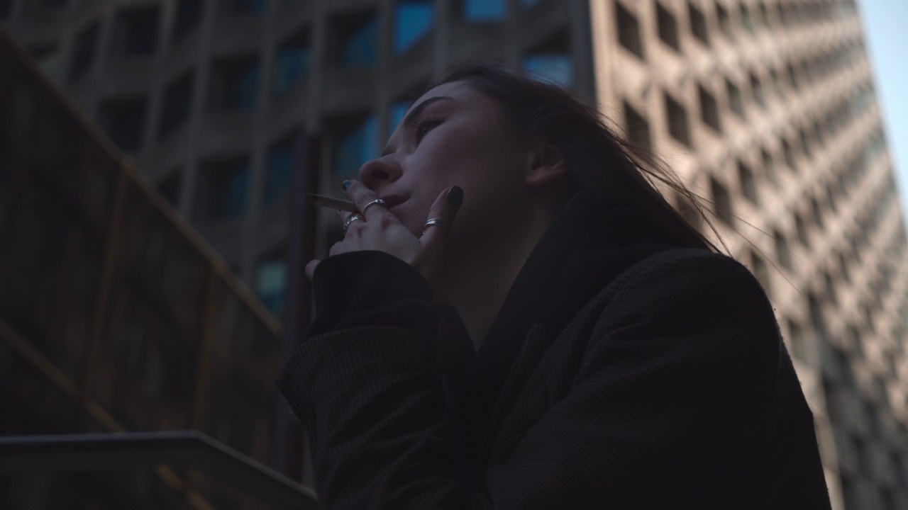 在阳光明媚的日子里，孤独的女人在大楼旁边抽烟的特写视频下载