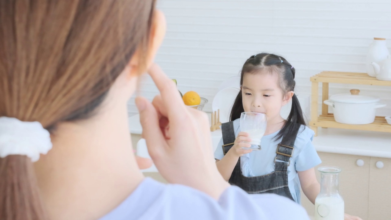 可爱的女儿和妈妈一起在厨房里喝牛奶，和家人一起呵护童年。视频素材