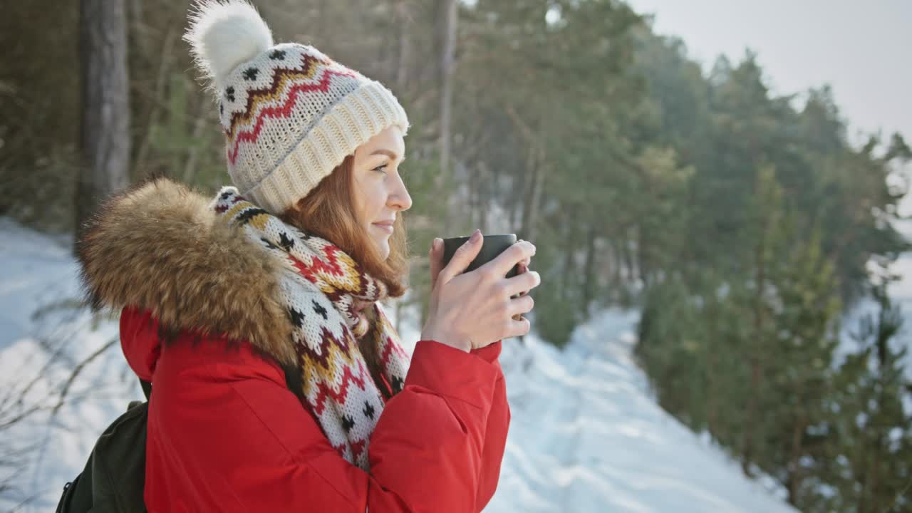 女子背包旅行者露营喝着热茶和放松在冬季森林，美丽的雪景在阳光明媚的日子。健康，真实，平衡感。4 K的视频视频素材